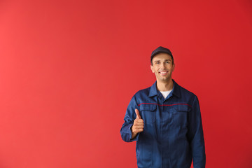 Male car mechanic showing thumb-up on color background