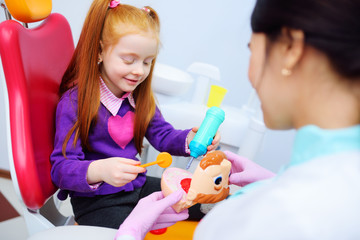 the baby is a little red-haired girl and a female pediatric dentist playing doctor with toy dental...