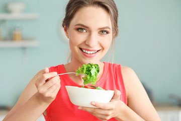 Young woman eating healthy vegetable salad in kitchen. Diet concept