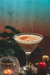 Traditional christmas eggnog with fir branch, burning candle, two balls on wooden background