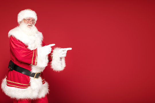 Real Santa Claus pointing on red studio background.