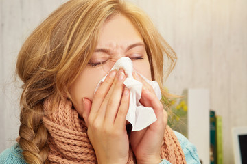 A blonde girl blows her nose in a handkerchief at home, against the background of a table on which lies an onion and lemons, books and a laptop