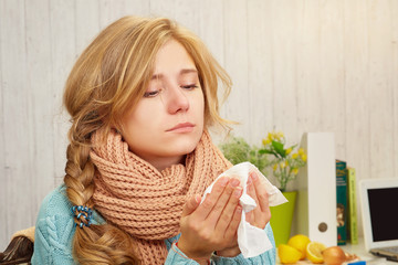 A blonde girl in a sweater looks in surprise in a handkerchief, on the background of a table, onions, lemons, a laptop and a book