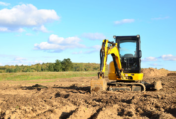 Mini excavator digging earth in a field or forest. Laying underground sewer pipes during the...