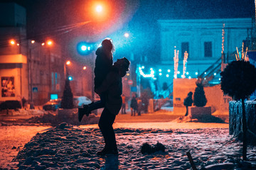 Young adult couple in each other's arms on snow covered street.