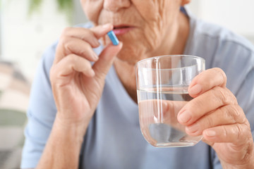 Elderly woman taking pill at home, closeup