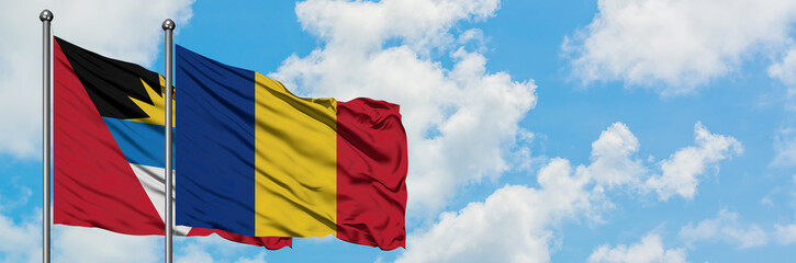 Obraz premium Antigua and Barbuda with Romania flag waving in the wind against white cloudy blue sky together. Diplomacy concept, international relations.
