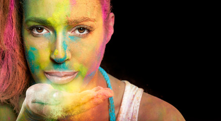 Beautiful woman covered in holi colors blowing colorful powder from her hand