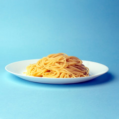 Spaghetti pasta on a white plate on a blue background. Creative, minimal concept