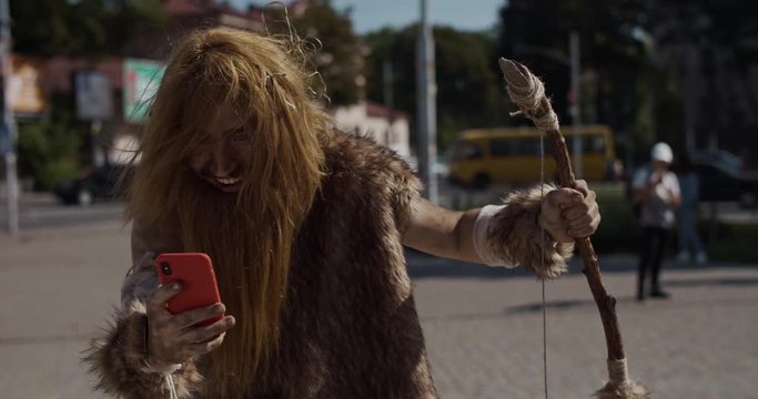 Smiling happy neanderthal of hunter-gatherers discovering modern device dance use mobile phone in modern city civilization cro-magnon evolution future homo sapiens human modern caveman slow motion
