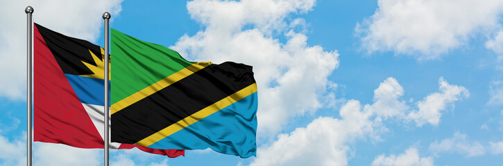 Antigua and Barbuda with Tanzania flag waving in the wind against white cloudy blue sky together. Diplomacy concept, international relations.