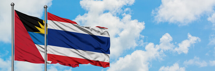 Antigua and Barbuda with Thailand flag waving in the wind against white cloudy blue sky together. Diplomacy concept, international relations.