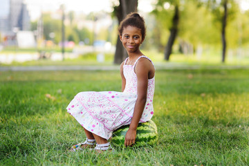 cute black African American girl sitting on a big watermelon in a Park on a Sunny summer day