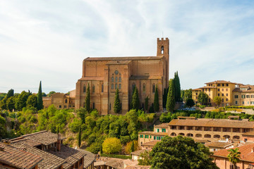 Scenic view of Siena cityscape over rooftops with San Domenico Basilica on background against blue sky. Tuscany, Italy