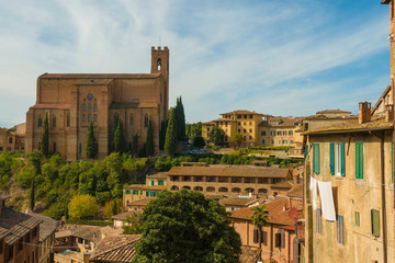 Scenic view of Siena cityscape over rooftops with San Domenico Basilica on background against blue sky. Tuscany, Italy