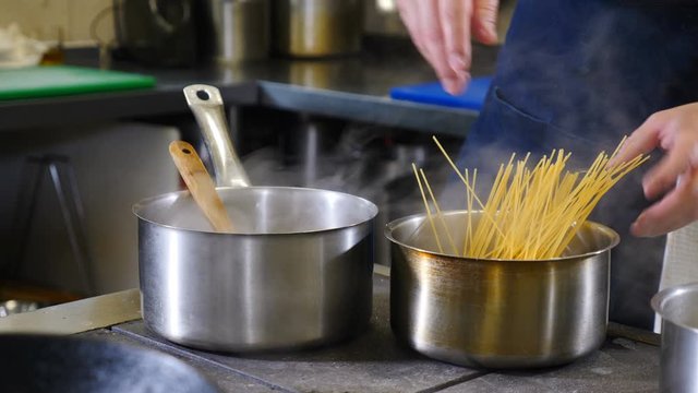 Busy restaurant kitchen concept. Team of chefs and kitchen staff preparing and serving food in commercial kitchen. Rush. Close up. Putting pasta into boiling water. Shot in 4k