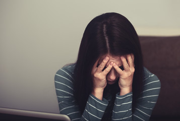 Unhappy crying young beautiful woman with headache sitting near the laptop. Closeup portrait of business person on work.