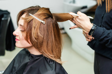 Naklejka premium Woman hairdresser is making hairstyle to red hair girl in beauty salon. The process of hair styling in the hairdressing salon.
