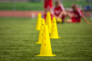 Yellow soccer training cones on grass field. Youth football players on training in the background....