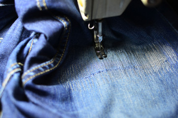 Stitching, stitching a hole in blue jeans with a sewing machine. Part of sewing machine and jeans cloth closeup. Tailoring - obrazy, fototapety, plakaty