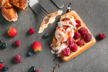 Tasty waffle with ice cream and berries on grey background