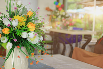Decorative plastic flowers in a white vase in a restaurant.