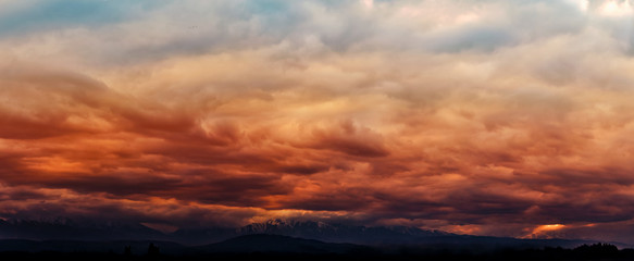 Naklejka na ściany i meble Dramatic light through the clouds against the backdrop of an exciting, vibrant stormy sky at sunset, dawn in the mountains. panorama, natural composition