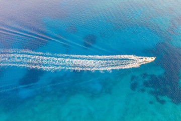 An aerial view of a boat speeding in  the beautiful Mediterranean sea, where you can se the rocky textured underwater corals and the clean turquoise water of blue lagoon Agia Napa