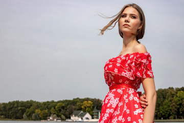 Portrait of a beautiful young brown-haired girl with long hair in a red dress on a lake background.