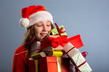 Joyful woman woman holding a lot of boxes with gifts on a gray background.