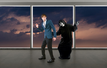 Man in a Halloween grim reaper ghost costume chasing, mocking and making fun of scared businessman...
