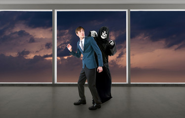 Man in a Halloween grim reaper ghost costume chasing, mocking and making fun of scared businessman...