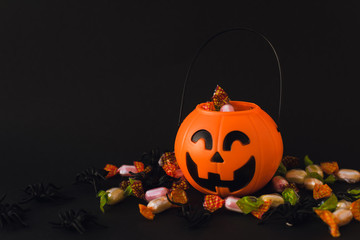 trick or treat for halloween. Pumpkin bucket with sweets and spiders on an black background. Sweets...