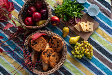 view from above of a table with fruits and cookies in wicker baskets and sliced cheese, sausage and a bunch of greenery