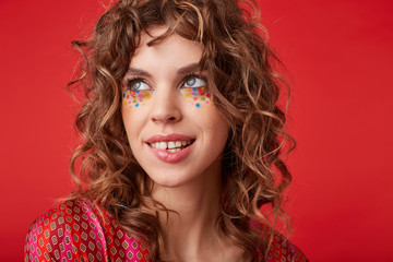 Beautiful young blue-eyed female with curly hair and with festive makeup looking aside with gentle...