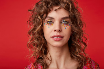 Studio shot of attractive young curly woman with multicolored dots on her face looking to camera...