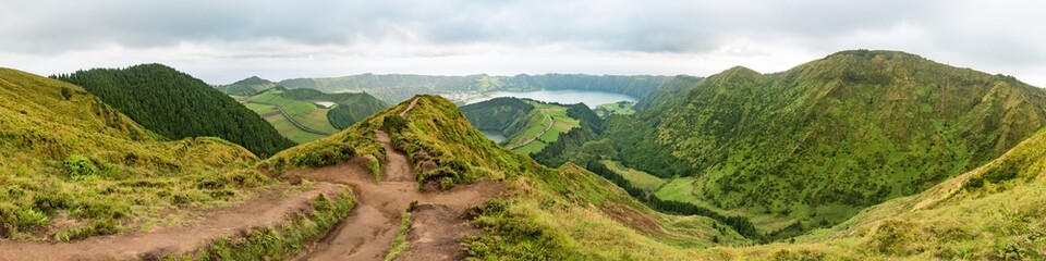 Fototapeta na wymiar Panoramic view from the Miradouro da Grota do Inferno viewpoint at Sete Cidades on São Miguel in the Azores. The Lagoa Azul is in the background with a mud dirt footpath leading towards the distance.
