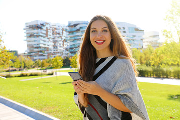 Young beautiful businesswoman smiling and looking at camera while holding mobile phone in her hand.