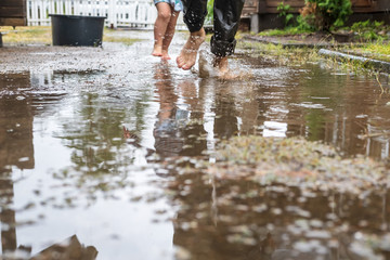 Mother and child have fun in the yard. They run barefoot through the puddles after a summer rain.