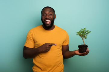 Happy boy indicates a small tree ready to be planted over a light blue color. Concept of...