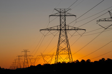 The sun rising behind a pair of towering electricity pylons