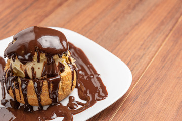 Profiteroles with ice cream and chocolate. Eclairs with black chocolate on wooden background. Traditional French dessert.