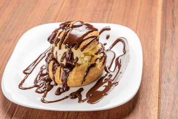 Profiteroles with ice cream and chocolate. Eclairs with black chocolate on wooden background. Traditional French dessert.