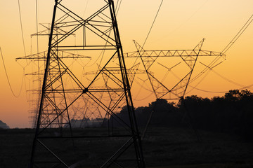 The sun rising behind a pair of towering electricity pylons