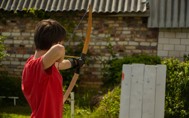 Archery boy bends bow archer target narrow in the summer field..