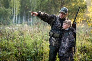 Father with gun showing something to son while hunting on a nature.