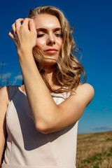 Portrait of a blonde young girl model who stands and poses on a sunny day against a background of haystacks and blue sky