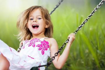 Little child blond girl having fun on a swing