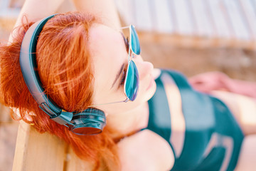 Beautiful woman listening to music on the beach. Red-haired girl resting on the beach, lying on a lounger and listening to relaxing music.