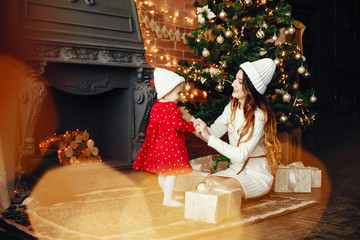 Naklejka na ściany i meble Elegant mother in a white sweater. Family with cristmas gifts. Little girl near christmas tree